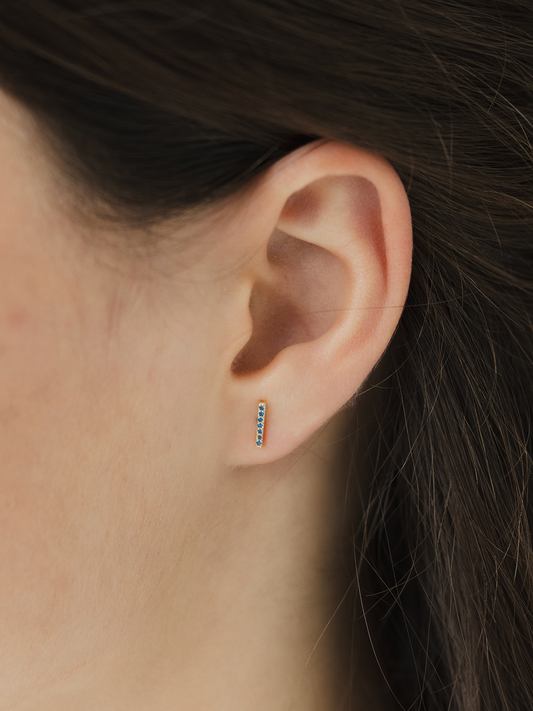 Close-up of an ear wearing a small birthstone cz earring with a blurred background