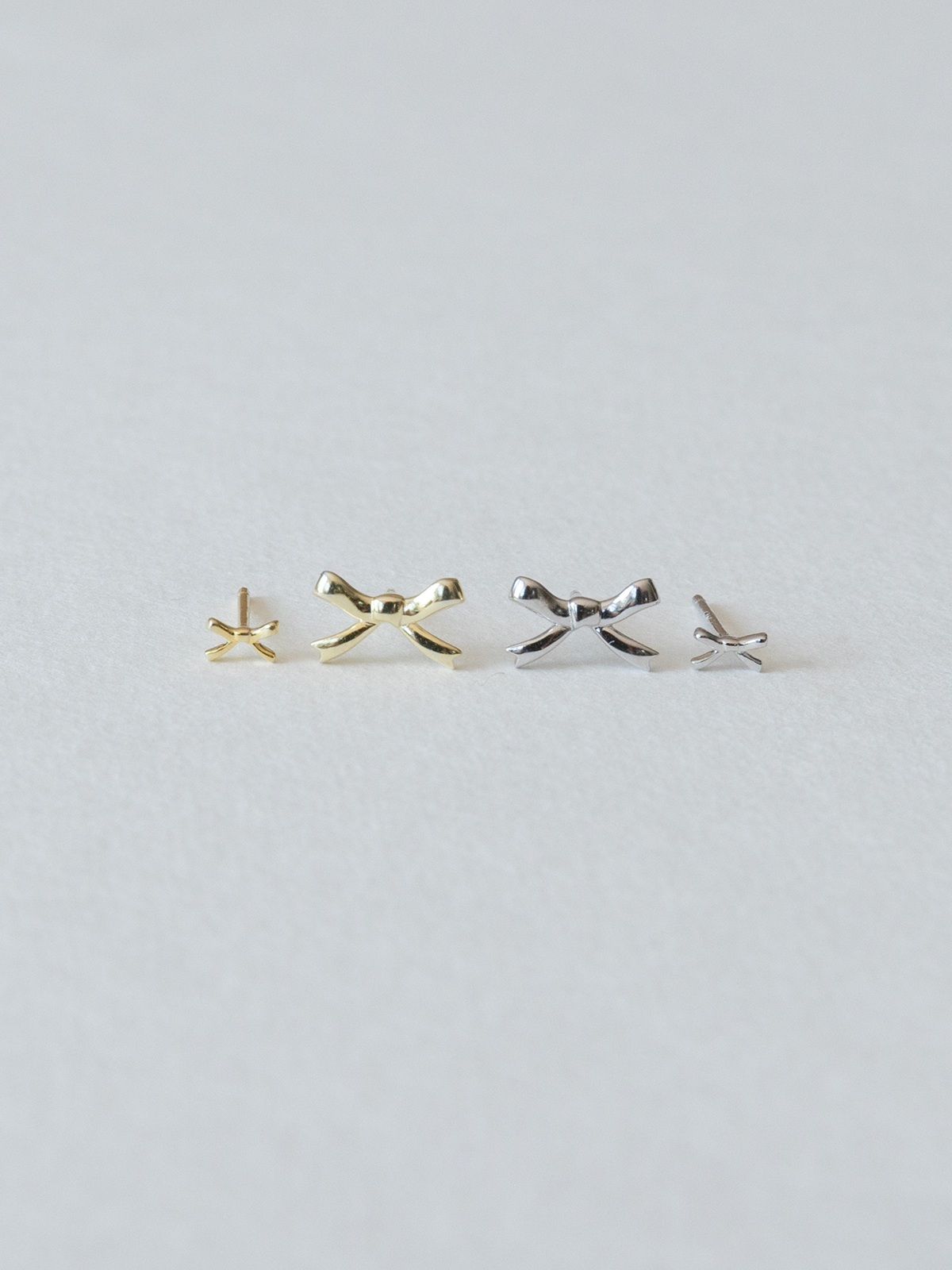 Pair of gold and silver bow-shaped earrings on a light gray background