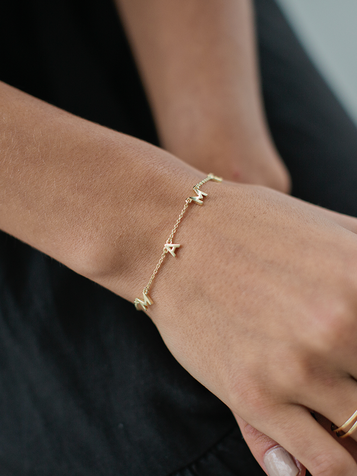 Gold bracelet with initial pendants on a wrist against a neutral background