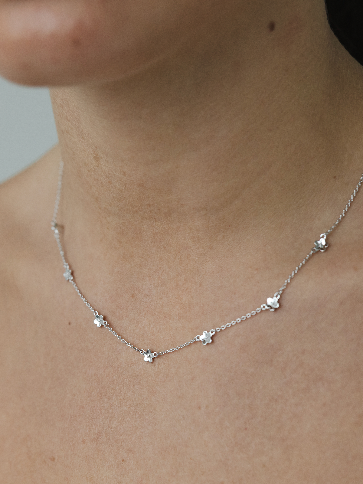 Silver necklace with small daisy pendants on a person's neck against a neutral background