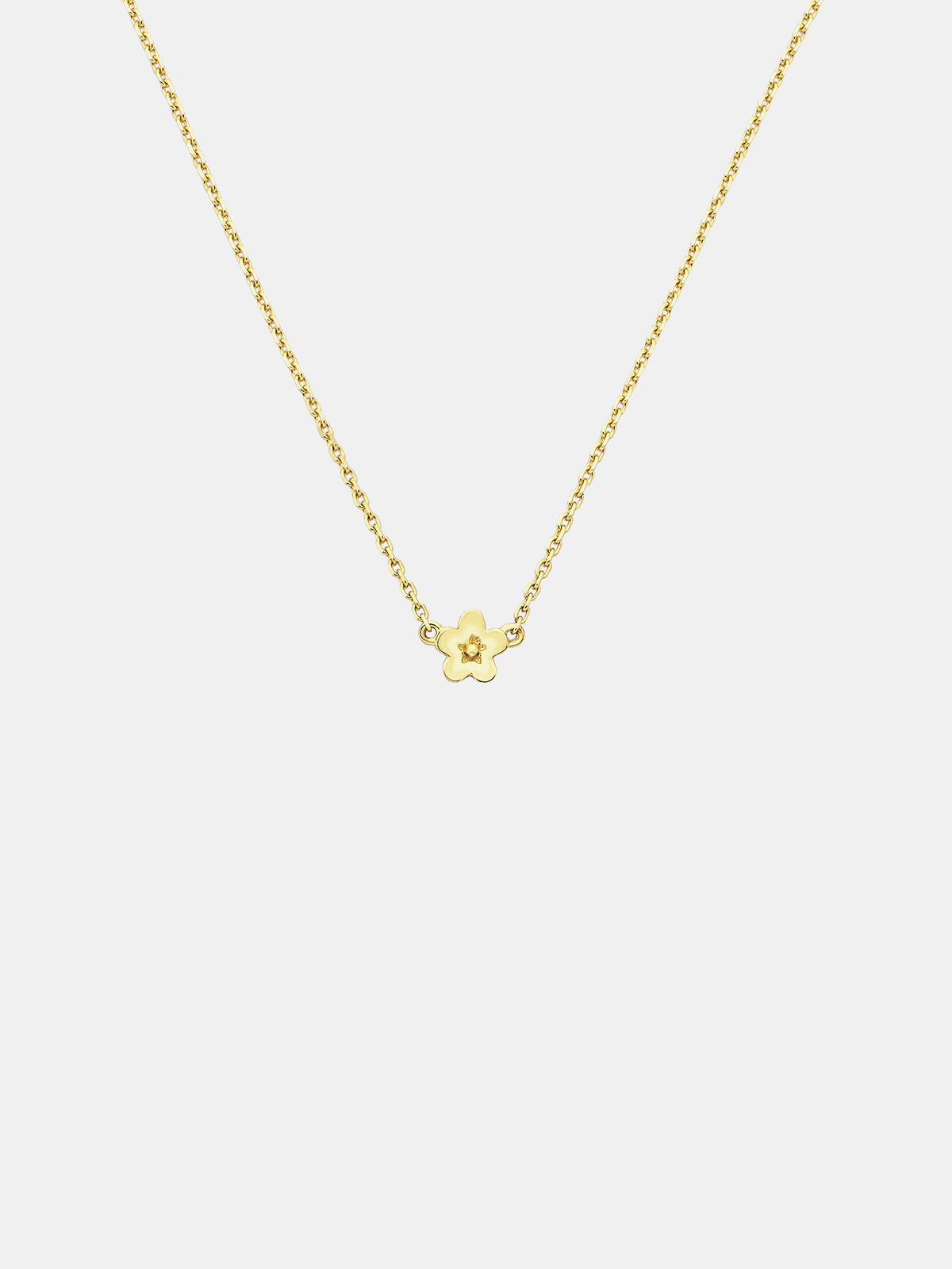 Solid gold necklace with a small daisy day flower pendant on a light grey background