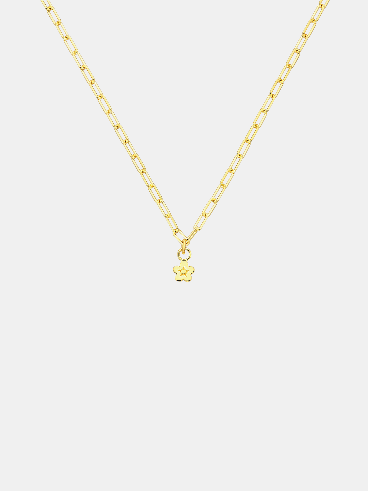Gold necklace with a daisy day flower pendant on a light gray background
