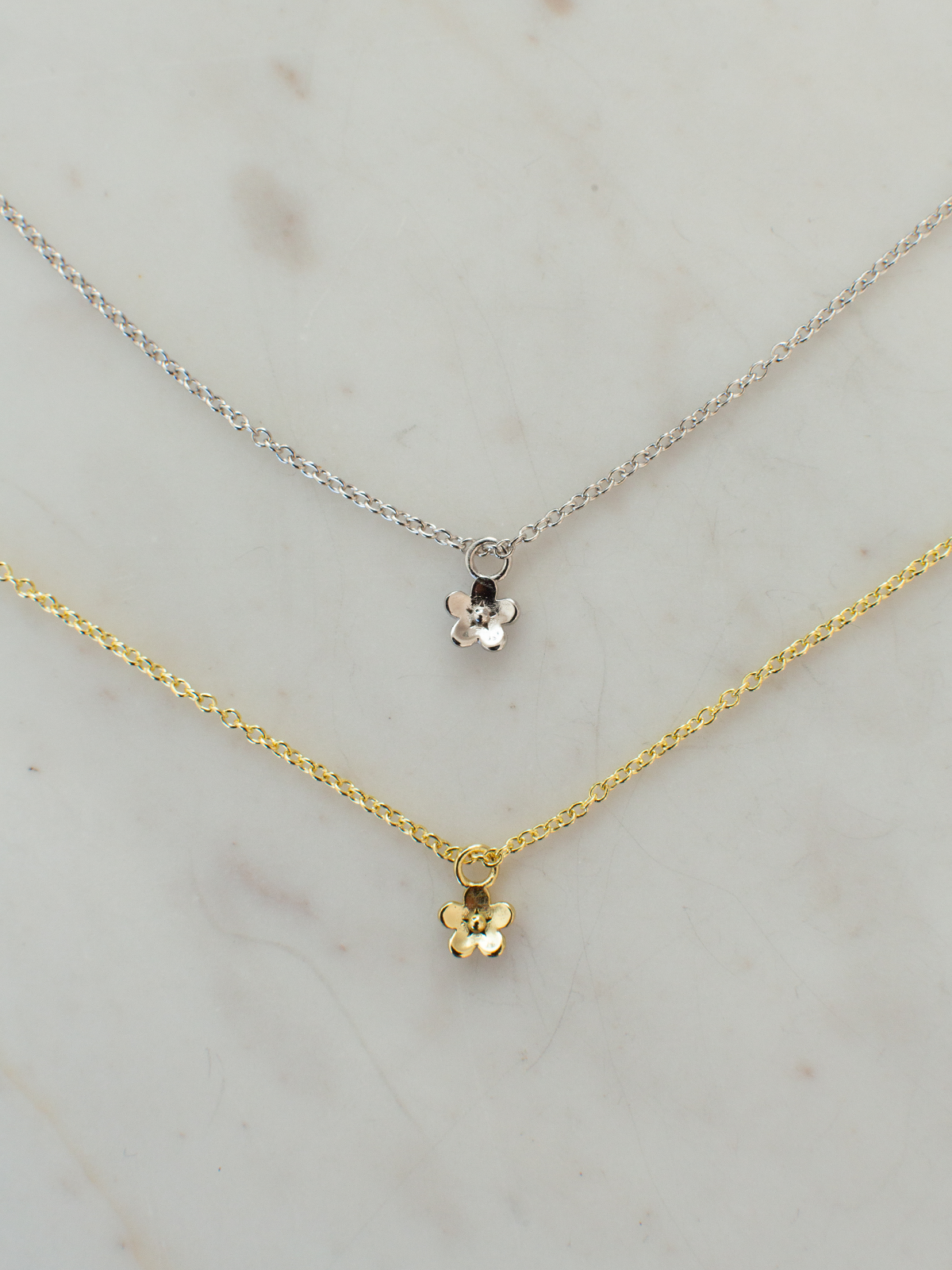 Two necklaces, one gold and one silver, on a light marble background