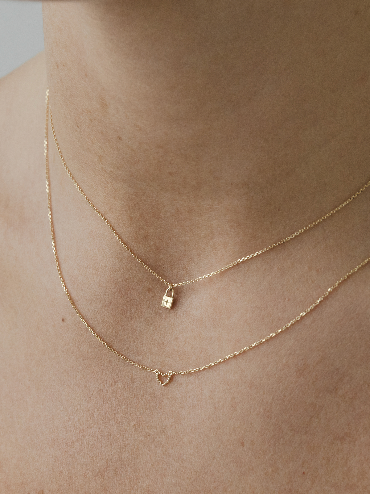 Two solid gold necklaces with lock and heart pendants on a person's neck.