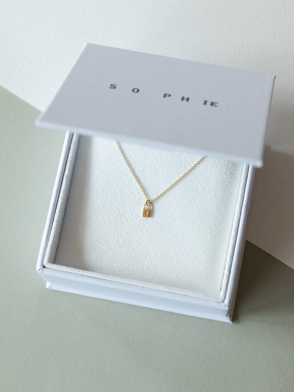 Solid gold little lock necklace in a white box with 'SOPHIE' branding on a light background