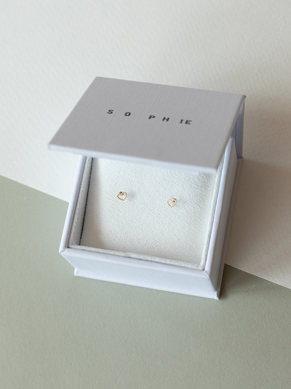 Solid gold dotty love heart shaped stud earrings in a 'SOPHIE' branded box on a light surface