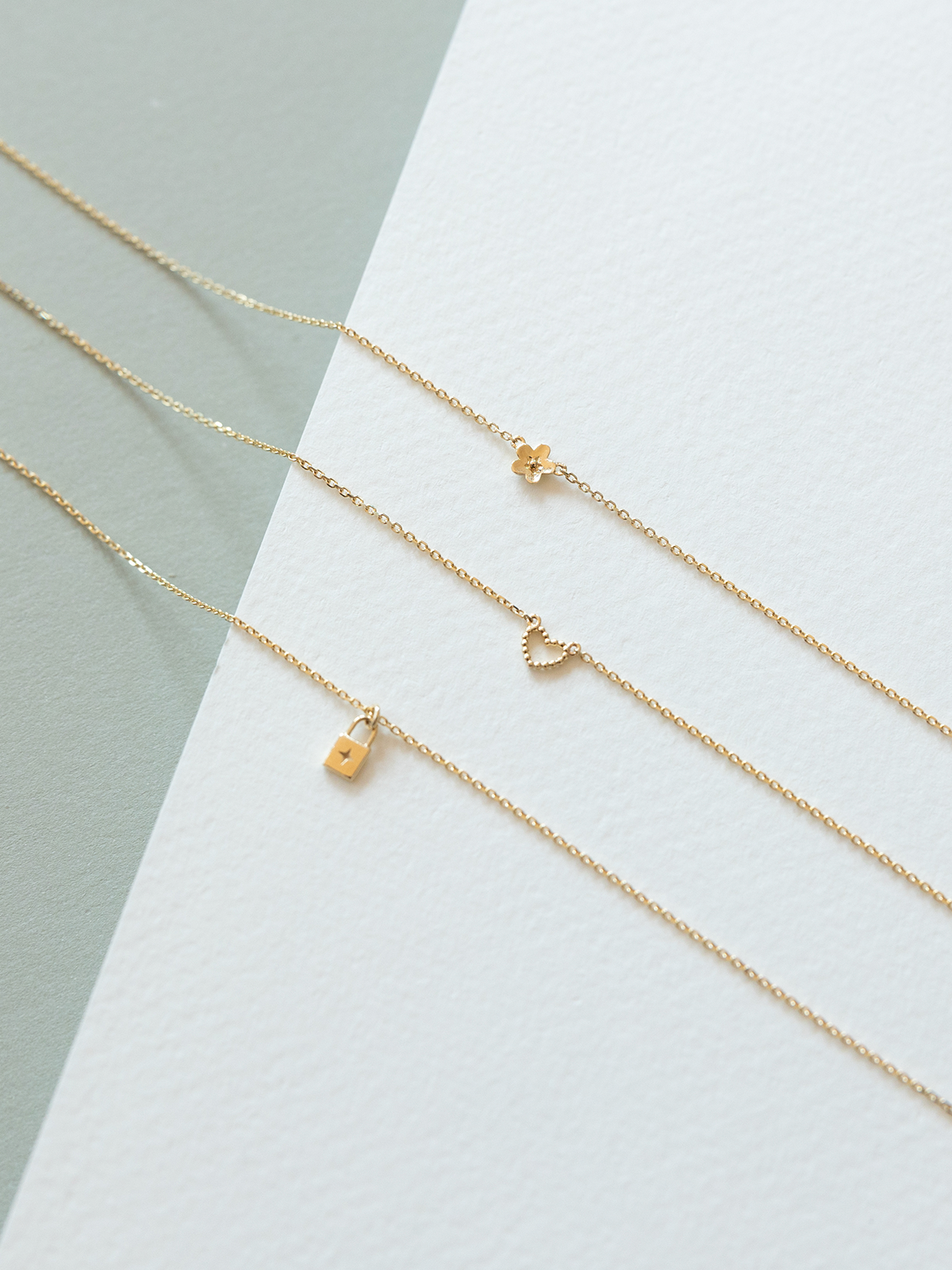 Three solid gold necklaces with SOPHIE iconic pendants on a light gray background