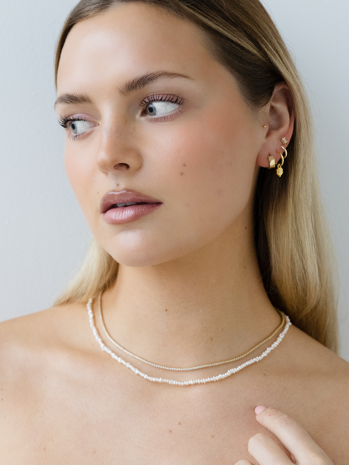 Woman wearing a pearl necklace and gold earrings against a plain background