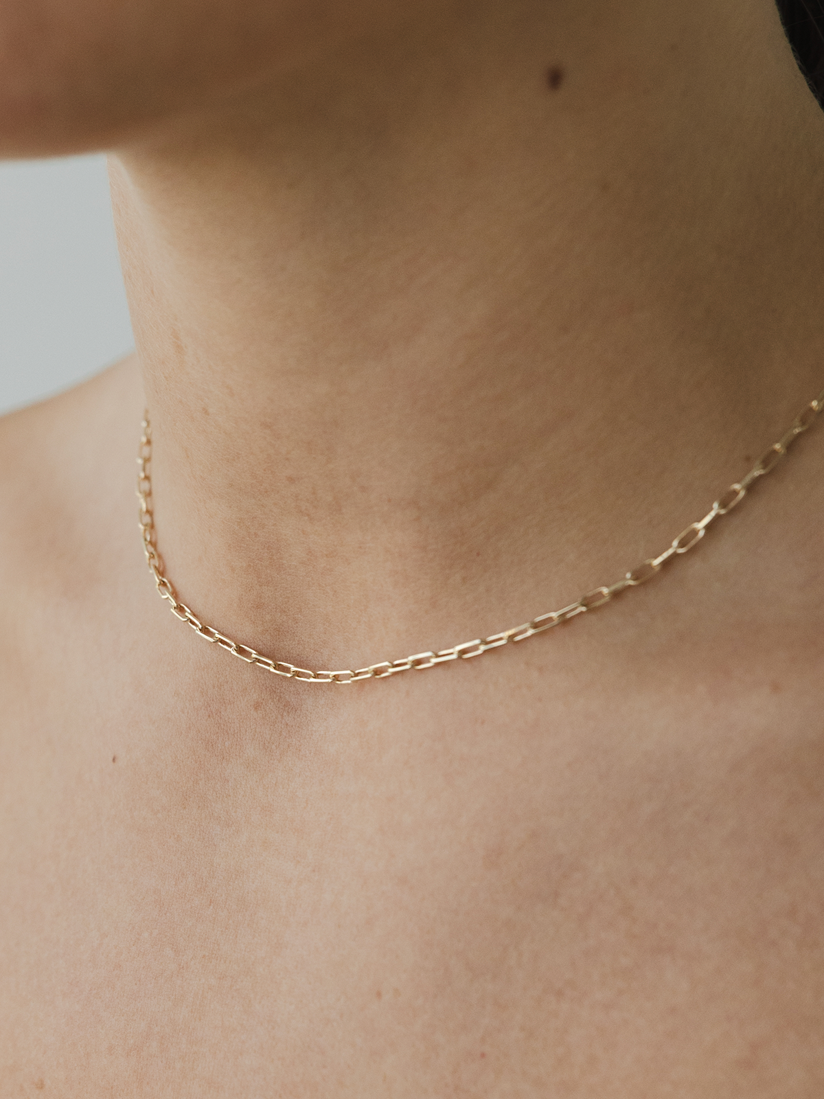 Gold chain necklace on a person's neck against a neutral background