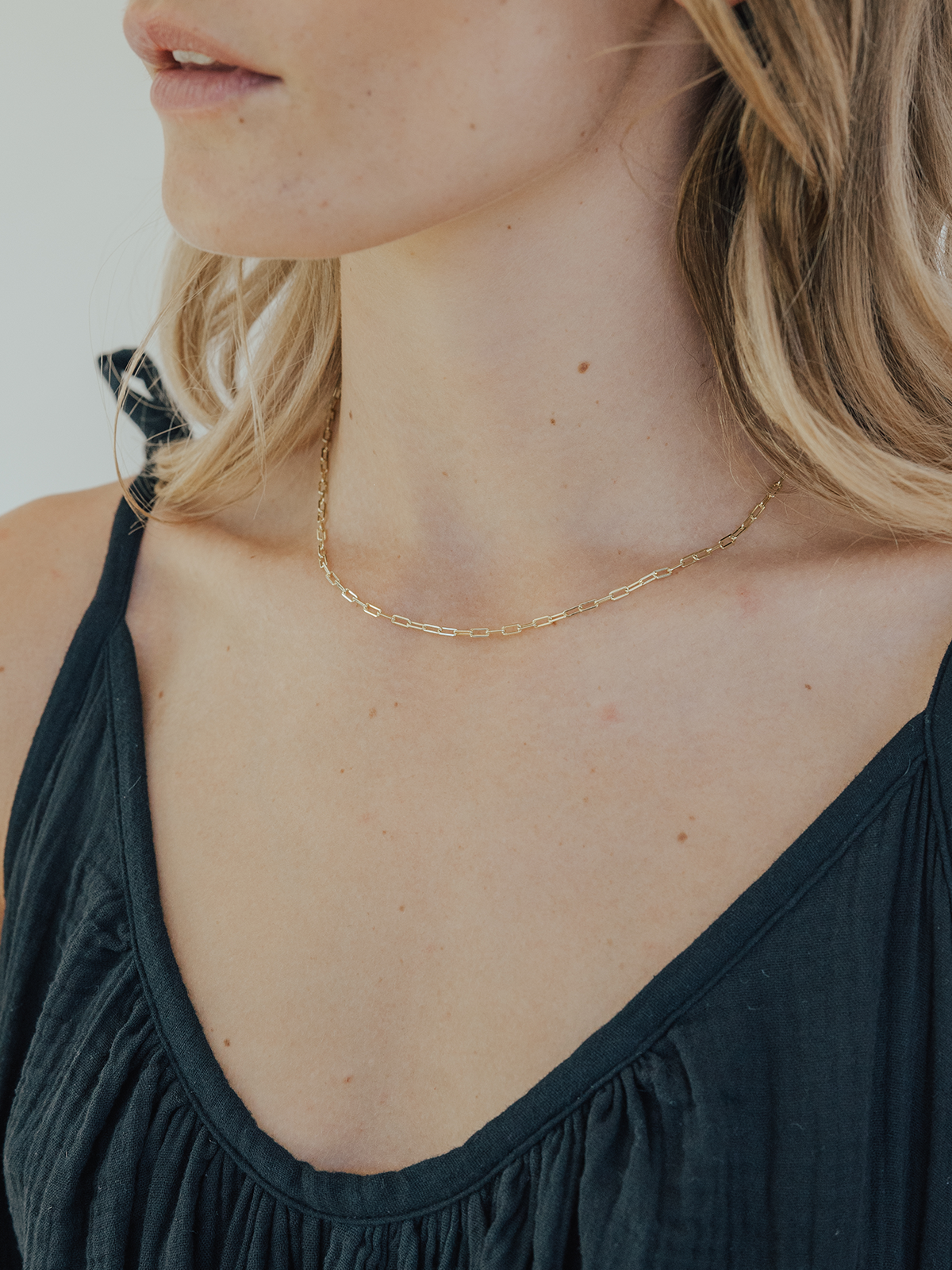 Woman wearing a gold necklace with a plain background