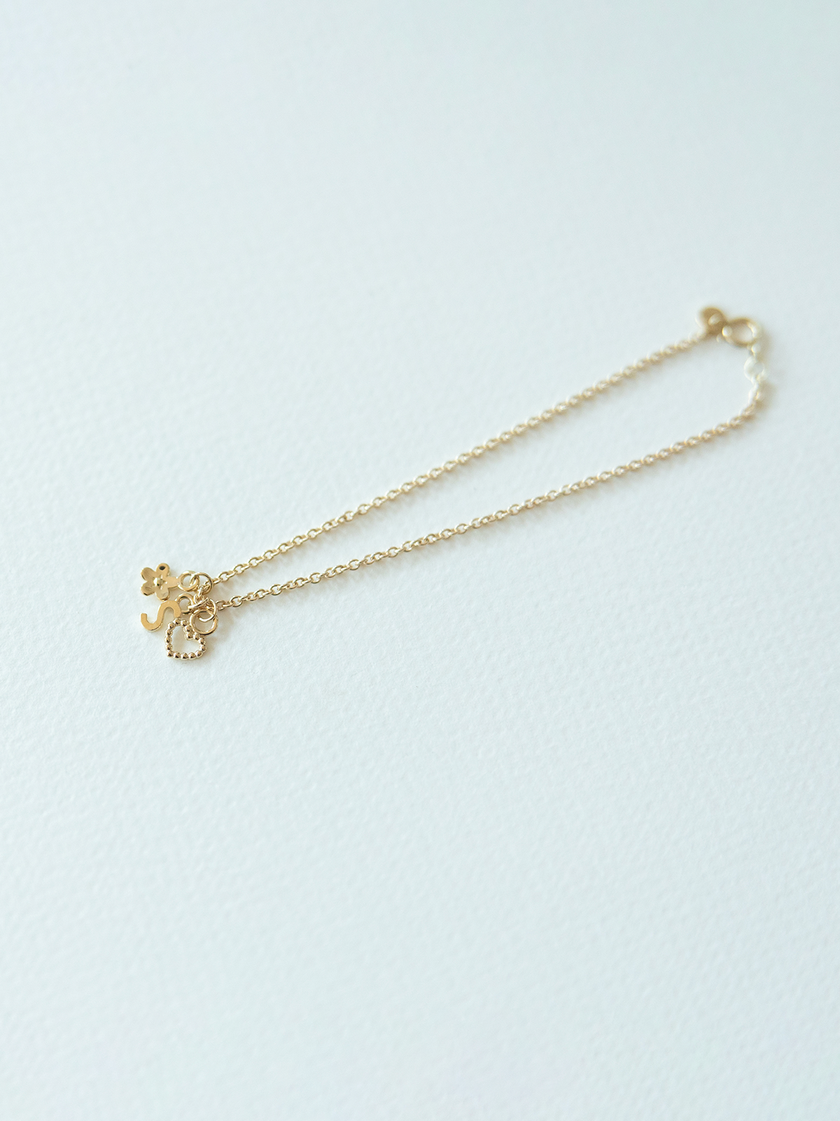 Solid gold mix it up bracelet on cable chain with a three small pendants on a light blue background