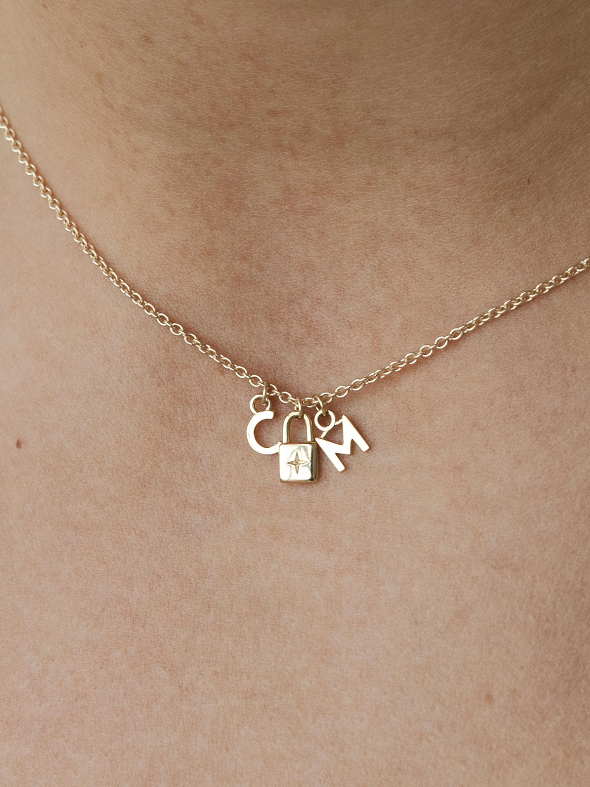 Gold necklace with lock and initials pendant on a beige background