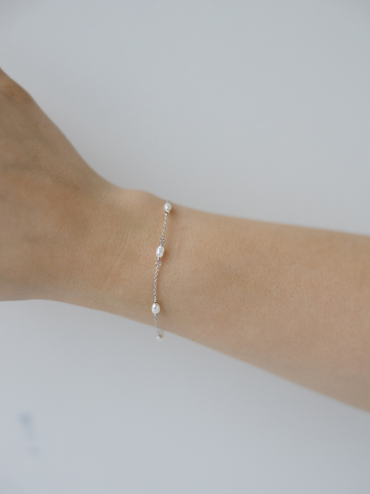 Silver bracelet with pearls on a wrist against a plain background