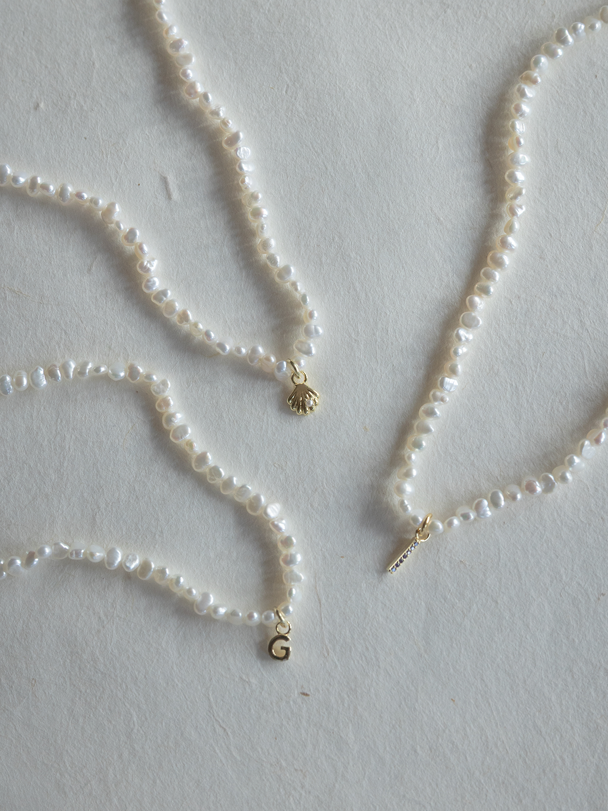 Three pearl necklaces with gold pendants on a light gray background