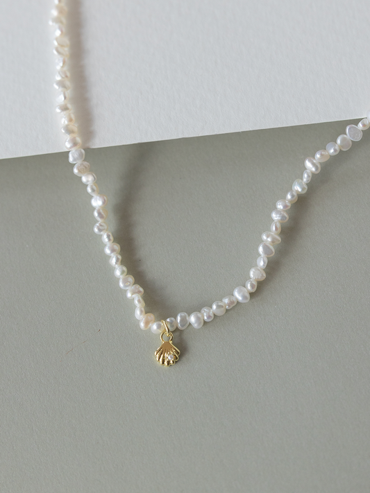Pearl necklace with a gold shell charm on a gray surface