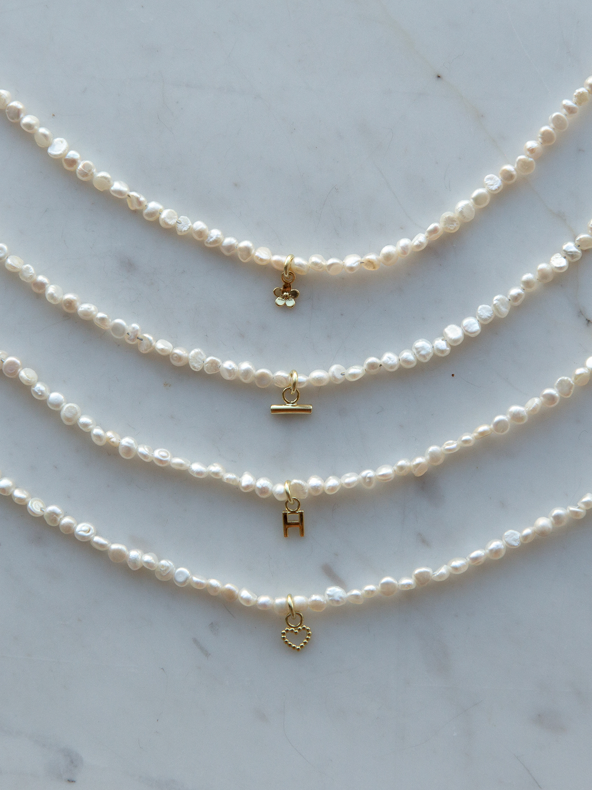Four pearl necklaces with gold charms on a marble surface
