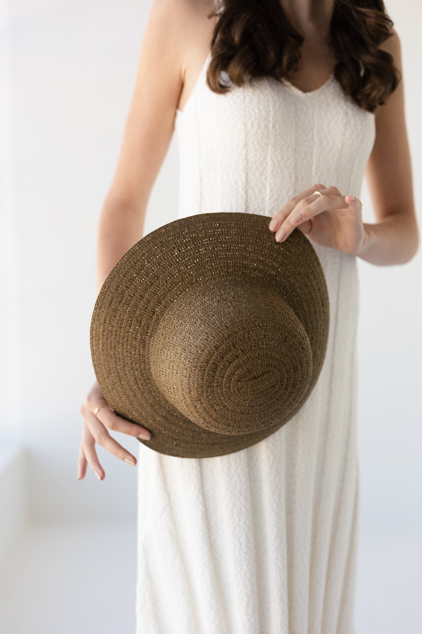 Woman holding a moss green straw hat against a white background