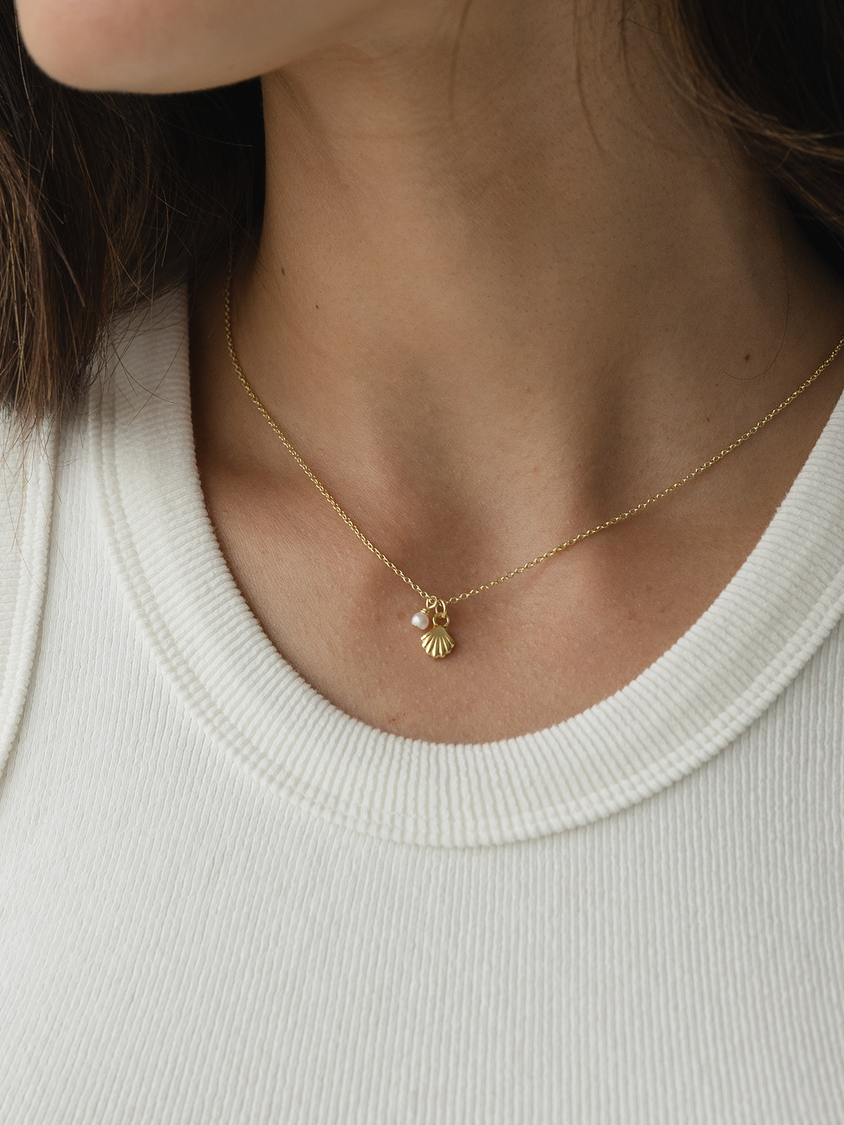 Gold necklace with a she shell pendant worn by a person against a white background