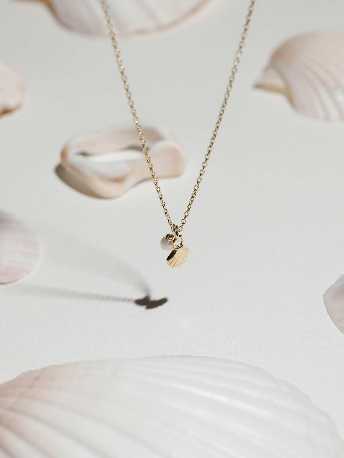 Gold necklace with a small shell & pearl pendant on a light background