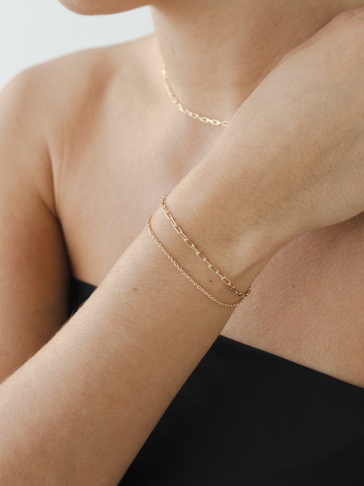 Close-up of a person wearing delicate solid gold bracelets on a plain background