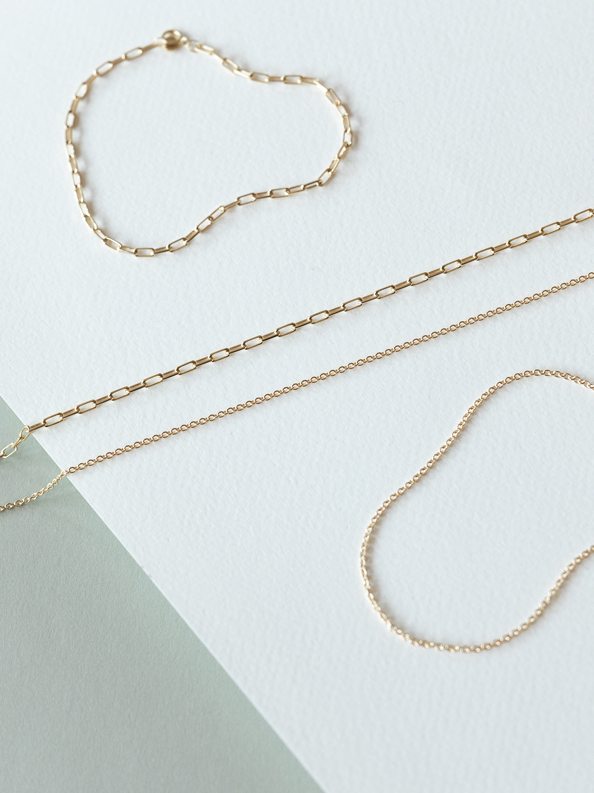 Mini links & cable chain solid gold bracelets & necklaces on a white & grey background