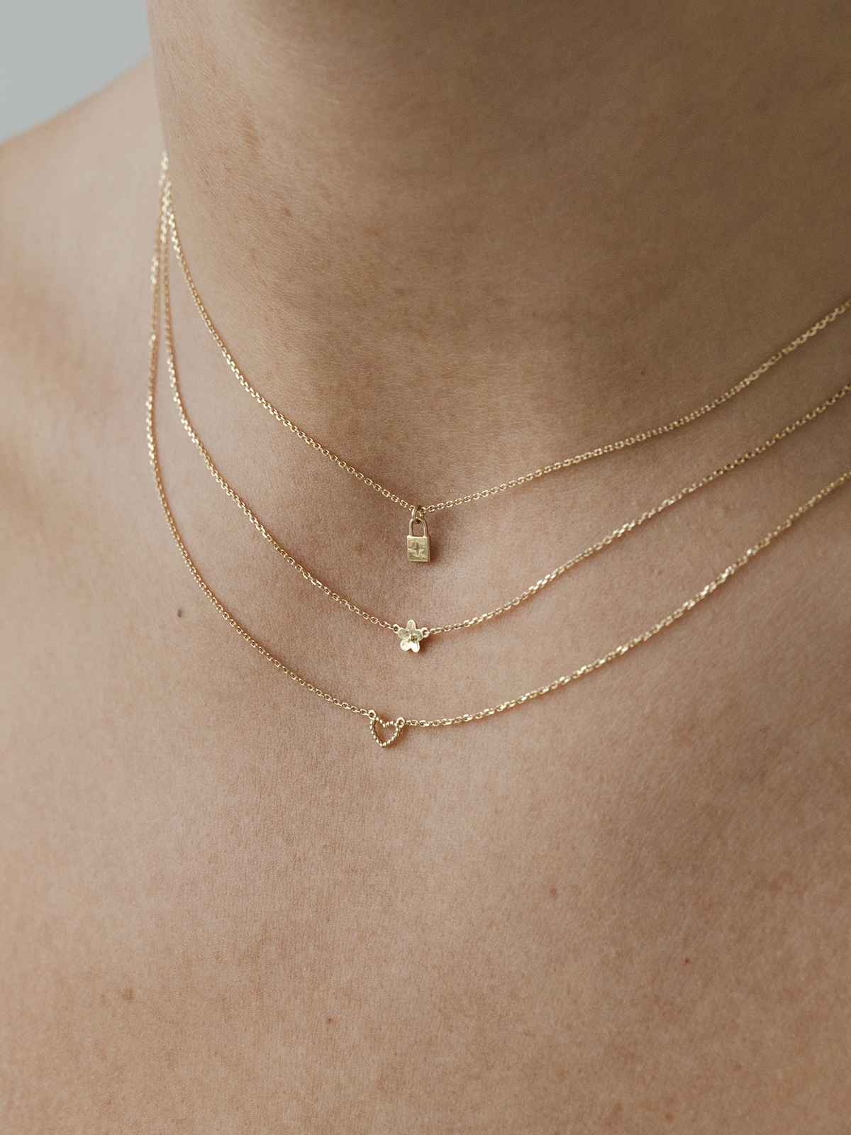 Three solid gold necklaces with dotty love heart, daisy day & little lock padlock pendants on a person's neck.