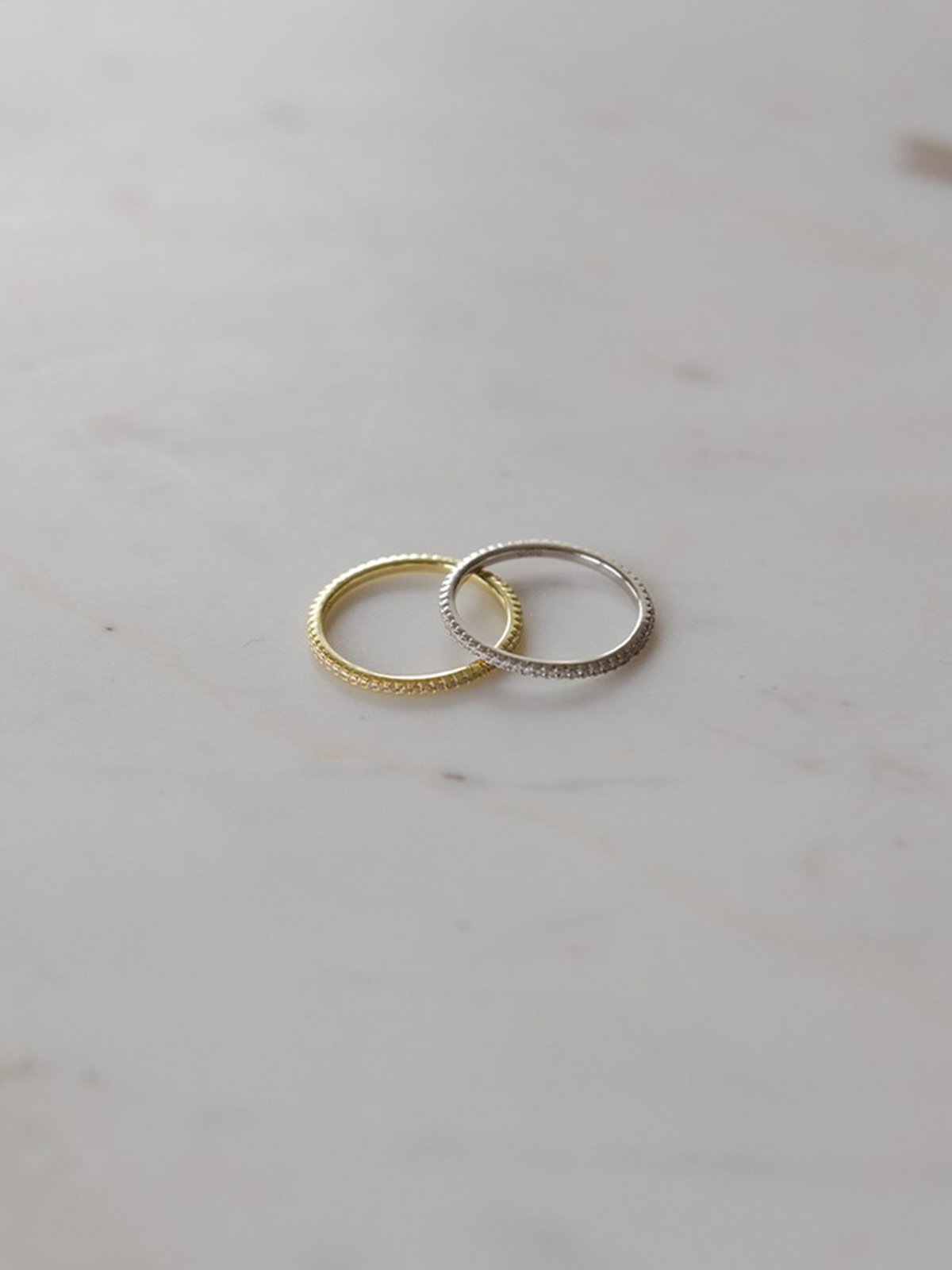 Two rings, one gold and one silver, on a light gray surface.