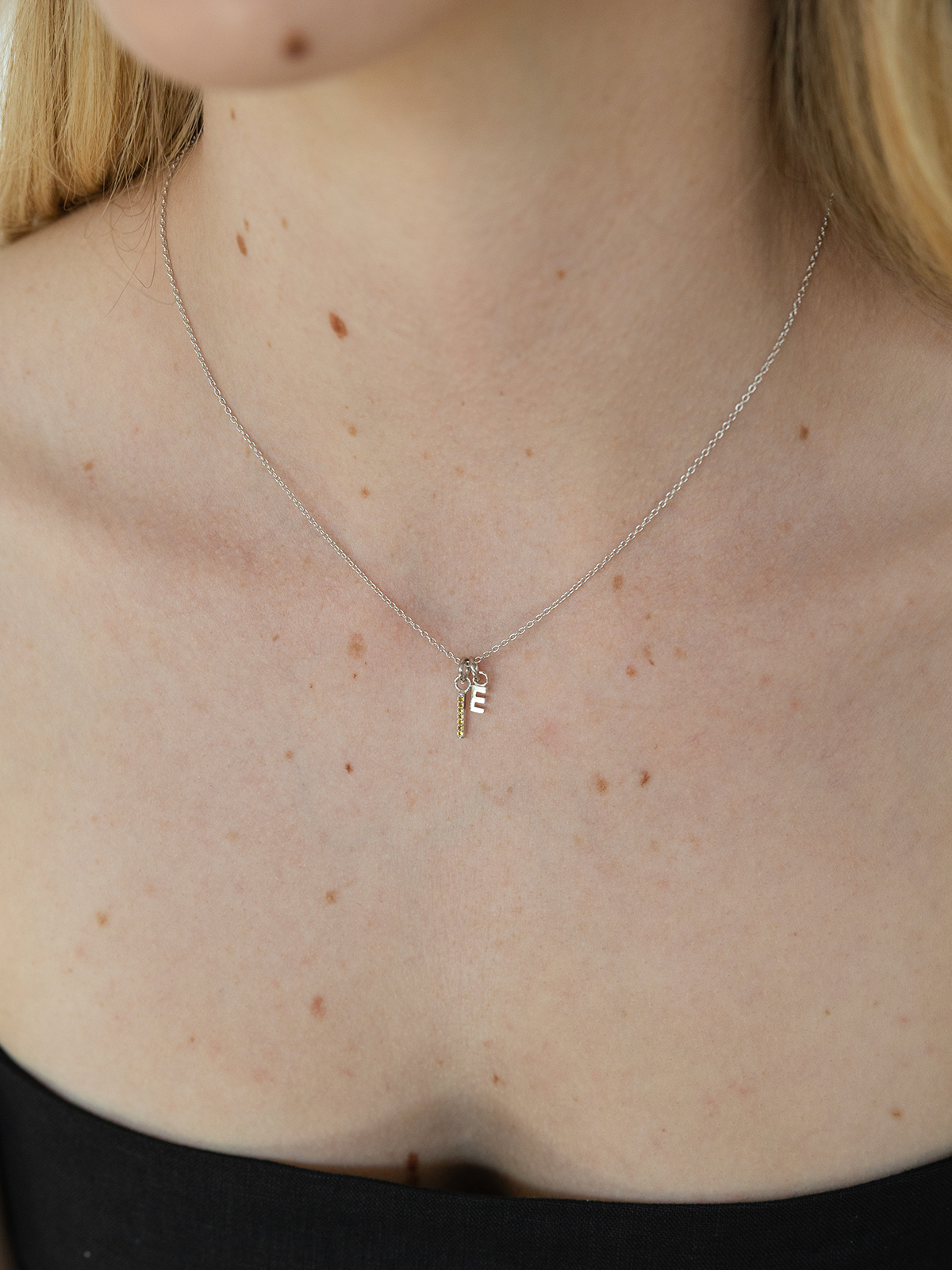 Necklace with a small birthstone & letter pendant on a person's neckline