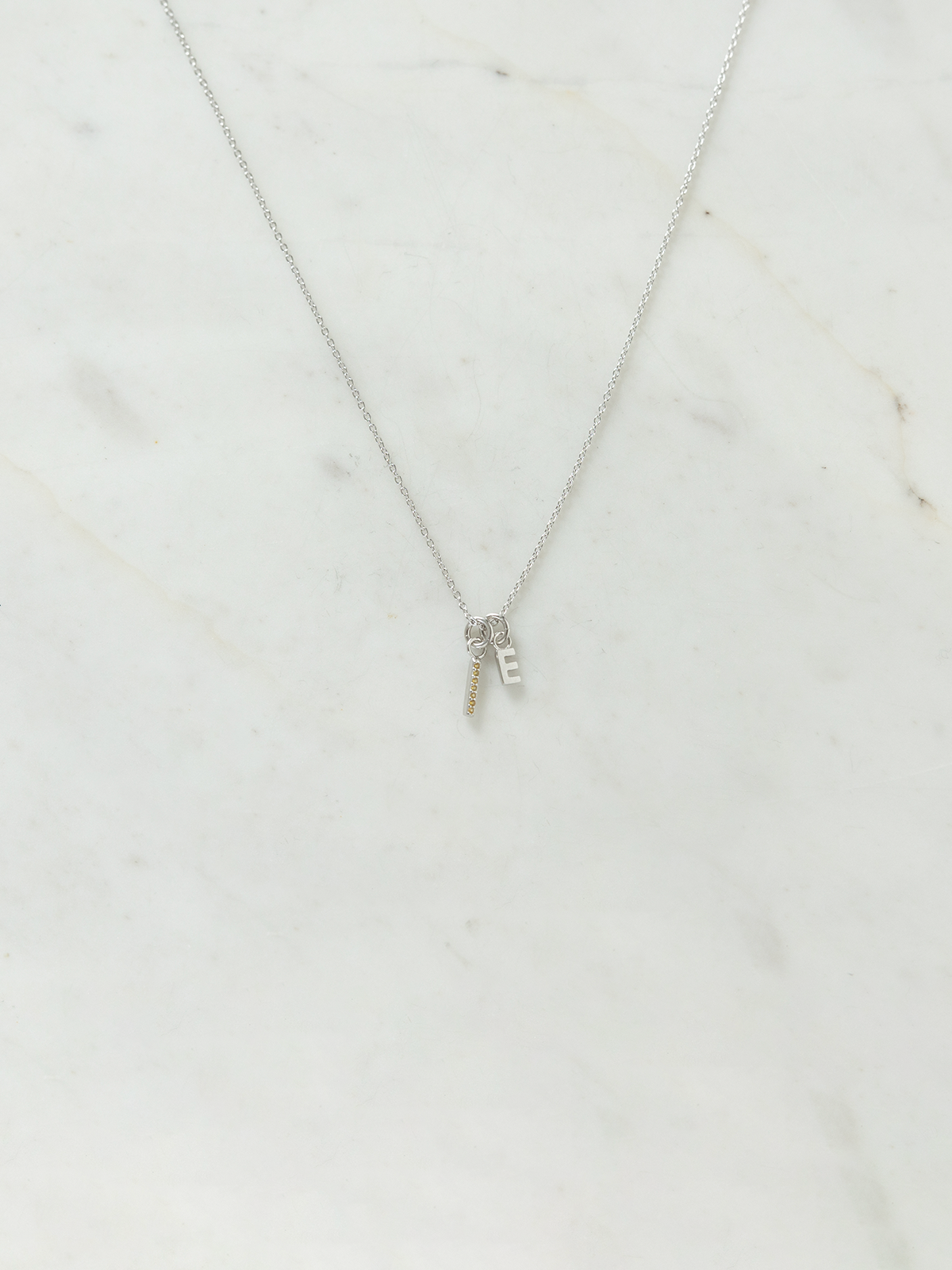 Silver necklace with a small birthstone & letter pendant on a marble surface