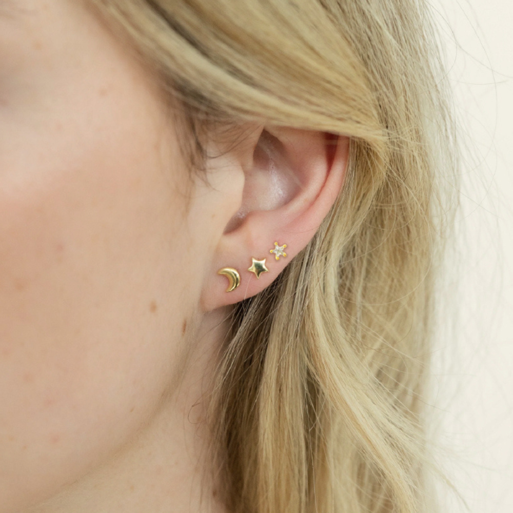 Close-up of an ear wearing gold earrings with a star and moon design.