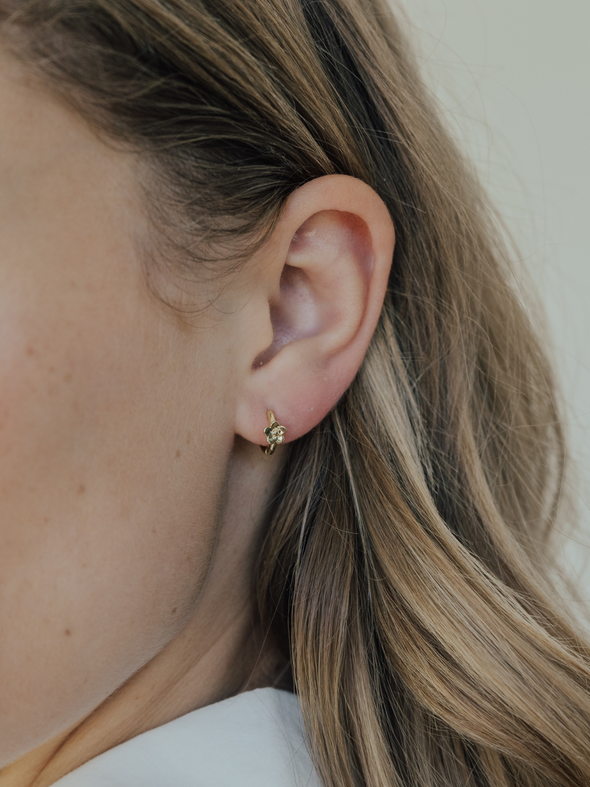 Close-up of an ear wearing a small gold earring with blonde hair.