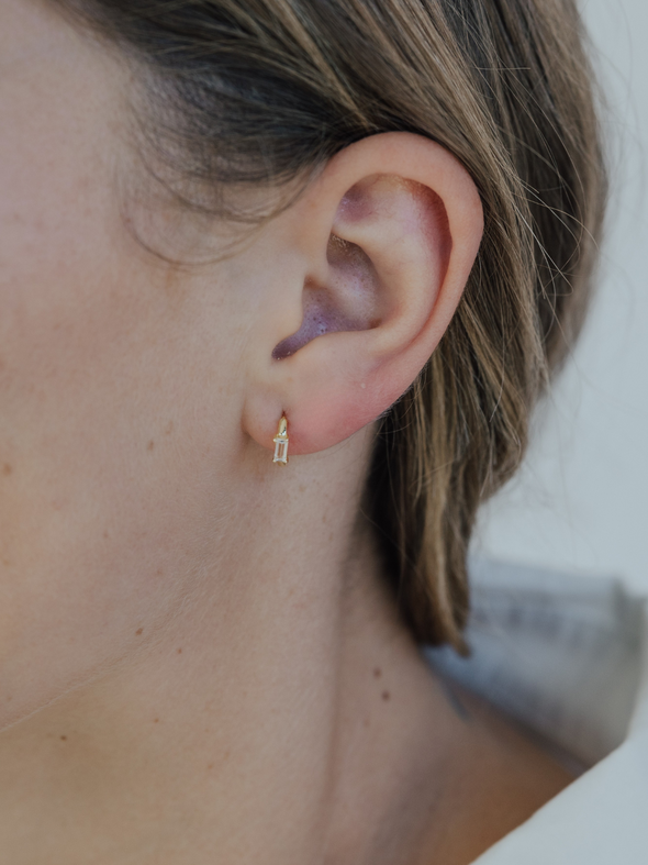 Close-up of an ear wearing a small gold earring with a blurred background