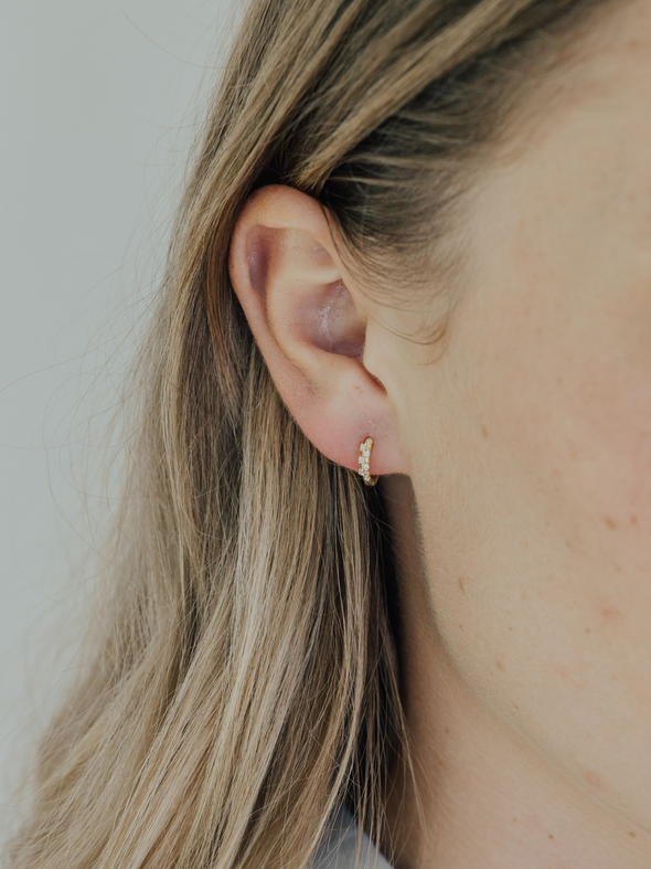 Close-up of an ear wearing a gold earring against a neutral background