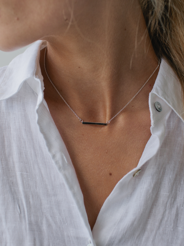Necklace with a minimalist design worn by a person in a white shirt.