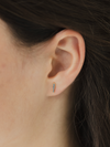 Close-up of an ear wearing a small birthstone cz earring with a blurred background