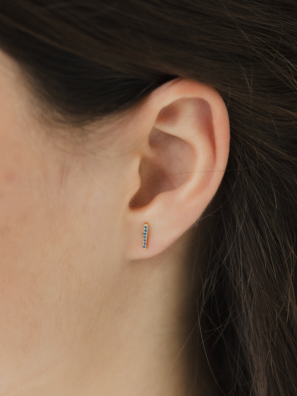 Close-up of an ear wearing a small birthstone cz earring with a blurred background