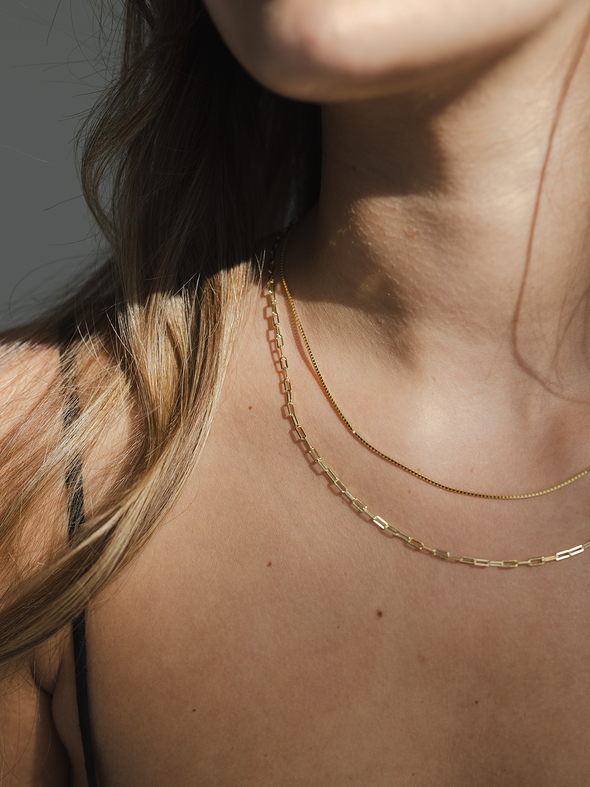 Close-up of a person wearing a delicate gold necklace against a neutral background