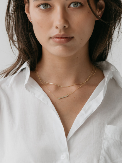 Gold box chain necklace stacked with the bar necklace on a model wearing a white shirt