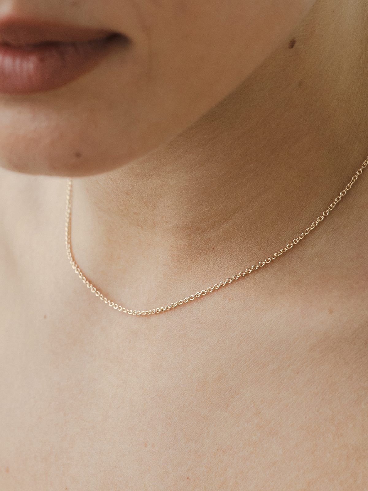 Cable chain solid gold necklace on a person's neck with a neutral background