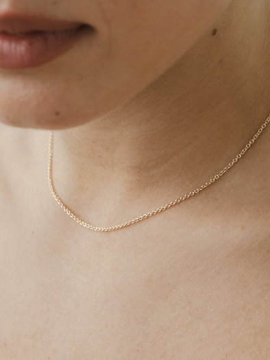 Cable chain solid gold necklace on a person's neck with a neutral background