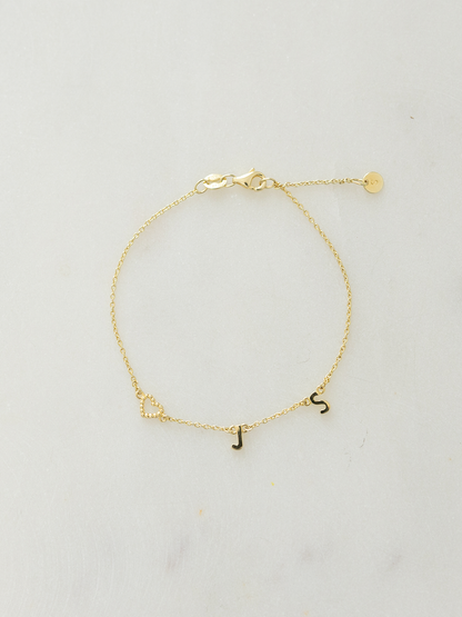 Gold choose your letters bracelet with the initials J, S & a dotty love heart pendant on a light gray background