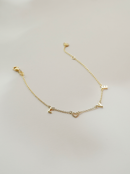 Gold bracelet with letter charms on a light gray background