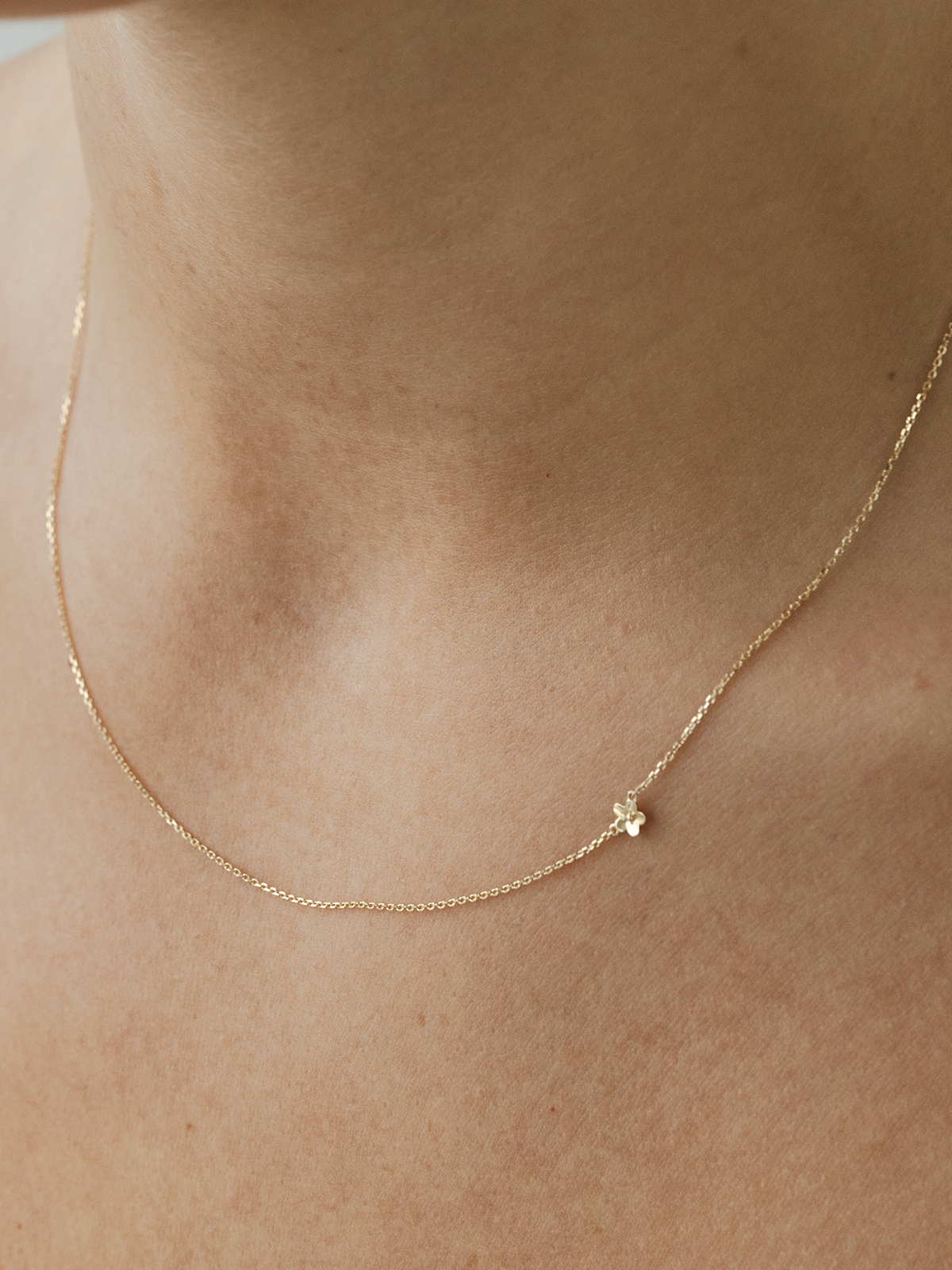 Solid gold necklace with a small flower pendant on a person's neck