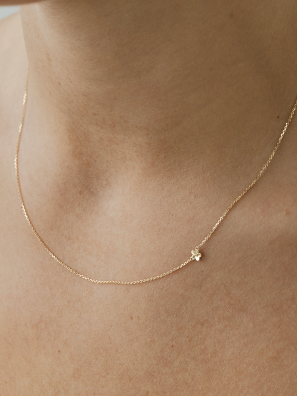 Solid gold necklace with a small flower pendant on a person's neck