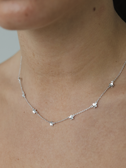 Silver necklace with small daisy pendants on a person's neck against a neutral background