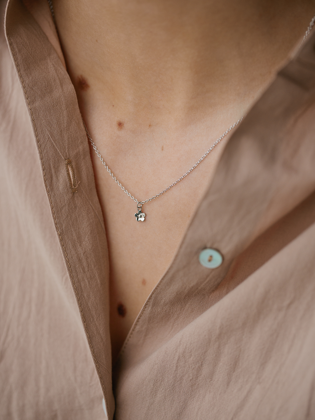 Necklace with a small daisy day pendant worn by a person wearing a beige shirt.
