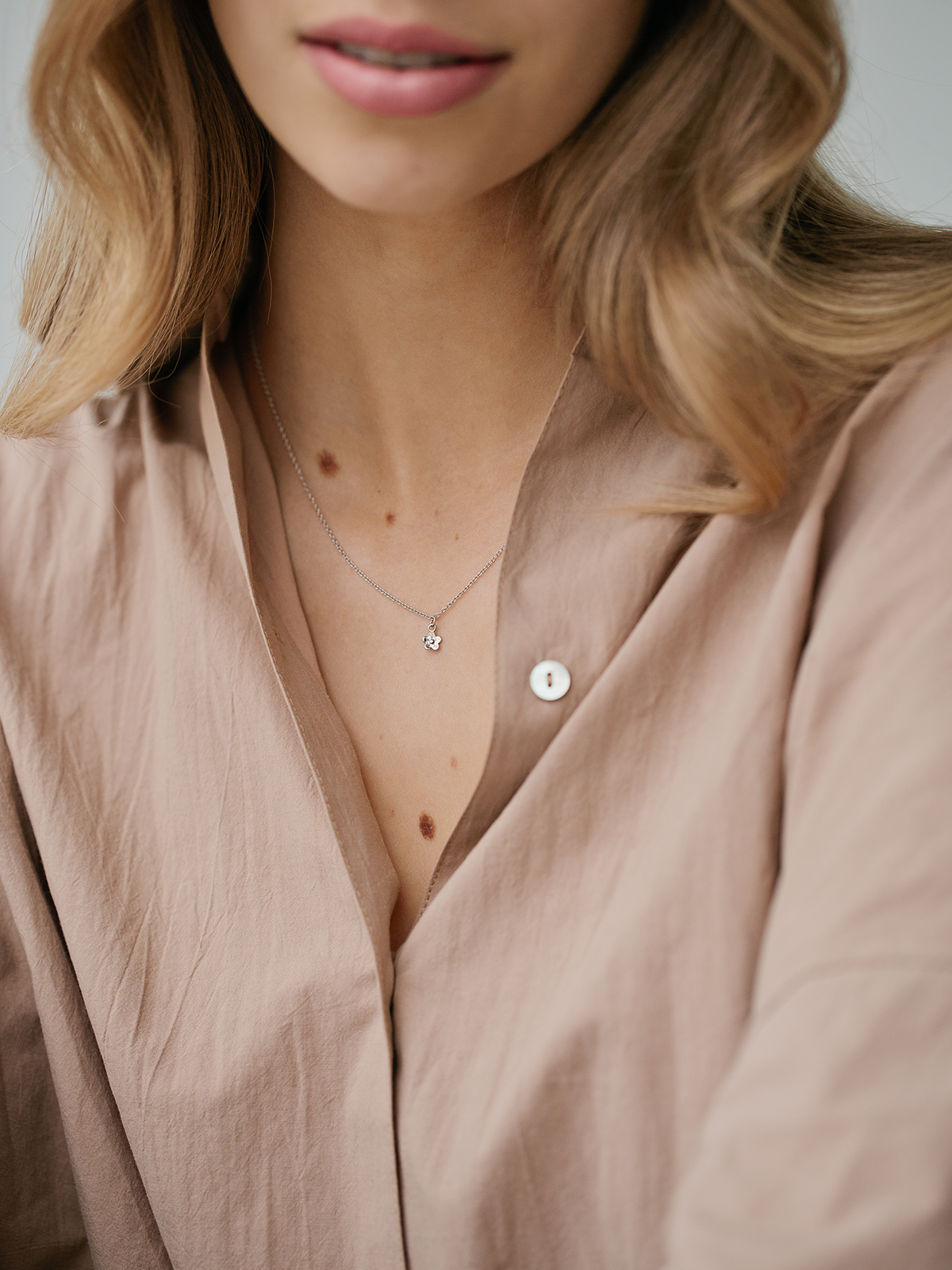 Close-up of a person wearing a light brown shirt with a necklace featuring the SOPHIE Daisy Day pendant