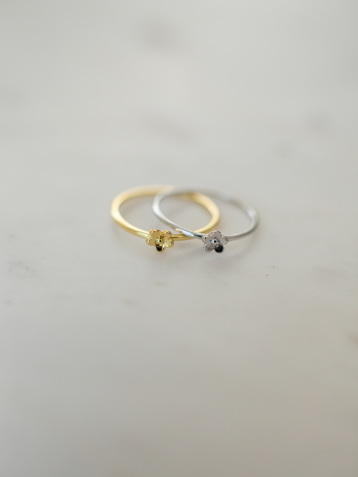 Two gold and silver rings with daisy pendants on a light gray background