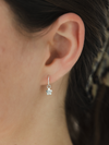 Close-up of an ear wearing a silver earring with a small daisy charm.