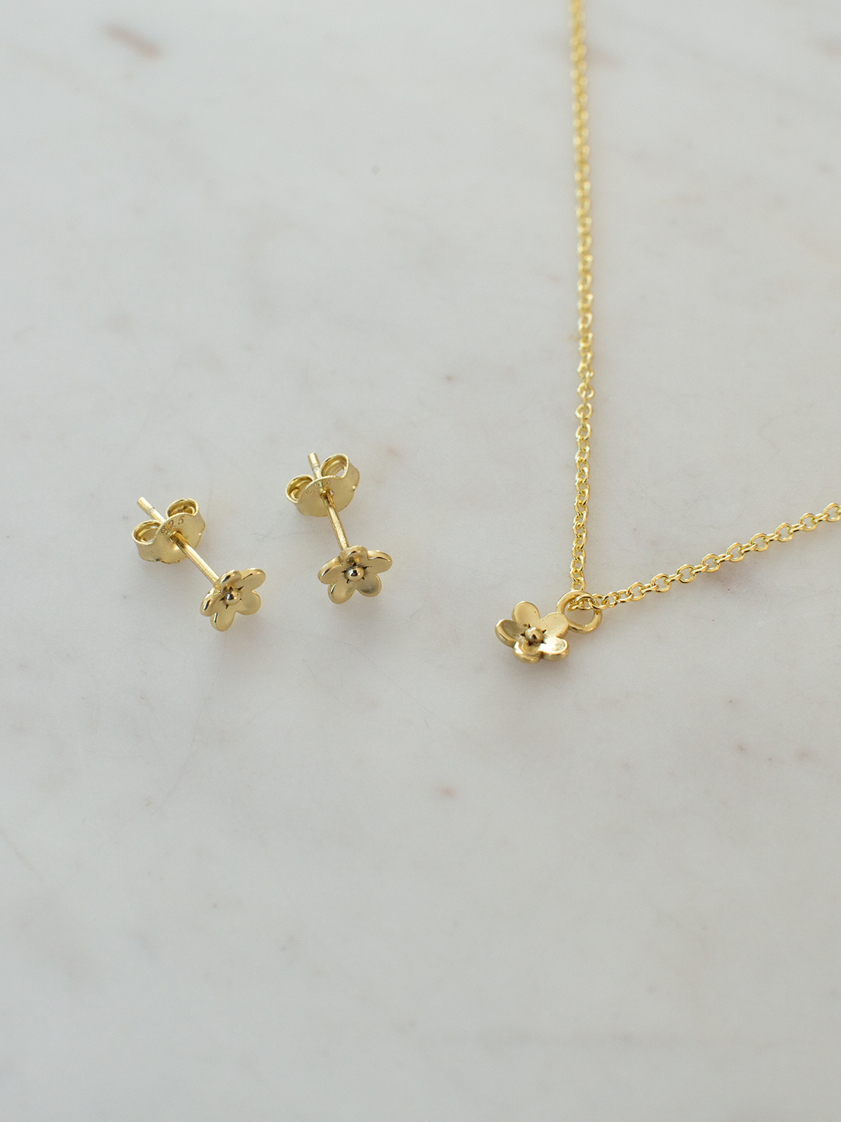 Gold flower-shaped earrings and necklace on a light gray background